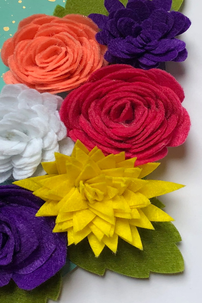 Rolled felt flowers in purple, pink, orange, yellow, white with green leaves