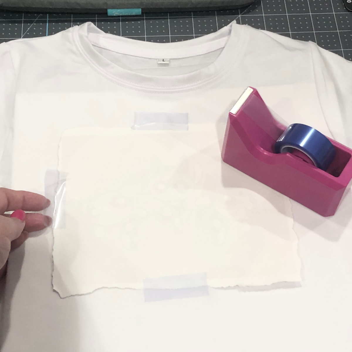white Cricut sublimation shirt with sublimation print face down on shirt with heat resistant tape and dispenser