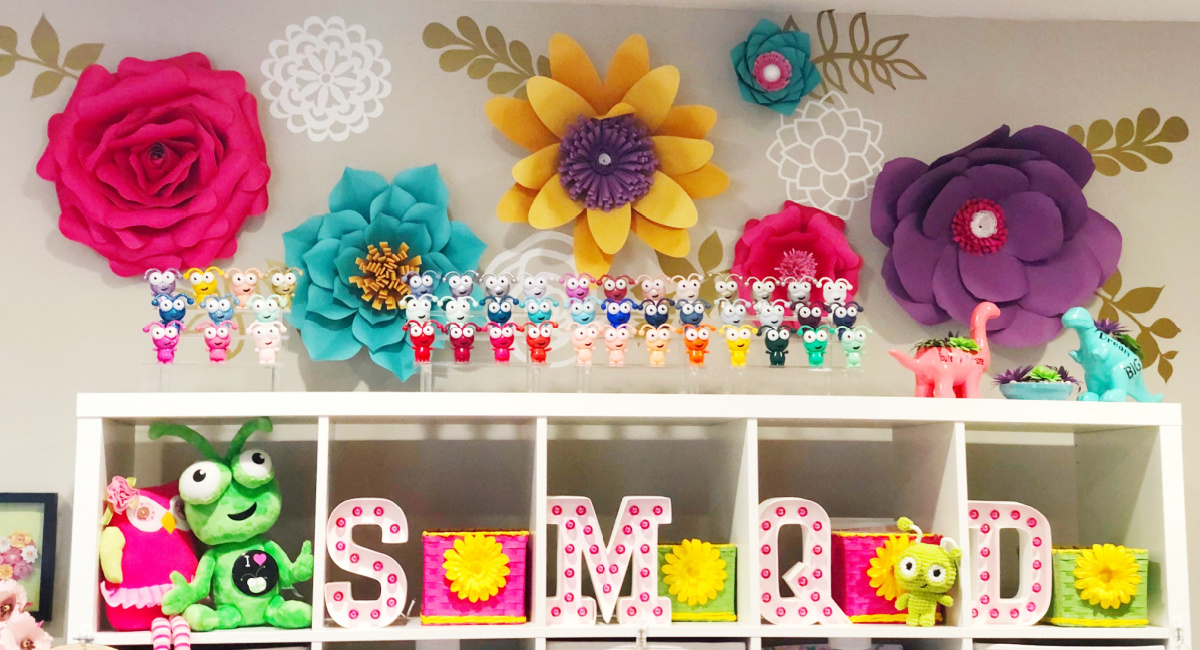 large paper flowers in pink, teal,yellow, purple on wall with gold leaves in vinyl and Cricut Cuties on acrylic stands